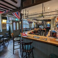 A bar area with wooden bar counter, stools, and a display of glasses.