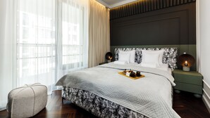 Ein modernes Hotelzimmer mit einem großen Bett, einem Nachttisch und einem Fenster mit transparenten Vorhängen.