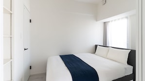 A modern, minimalist bedroom with a large bed, white walls, and a window with curtains. - BON Osaka West (Osaka)