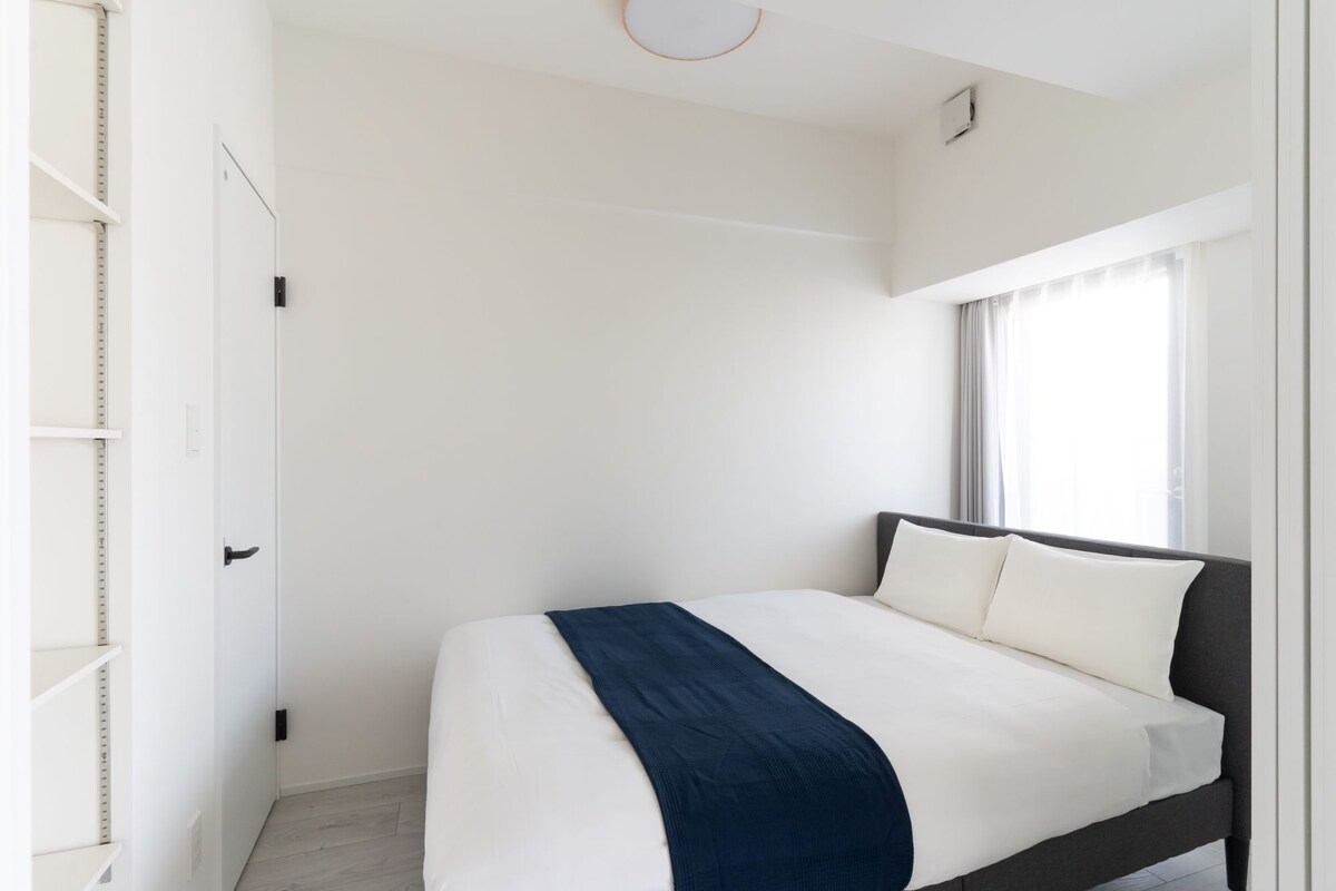 Une chambre à coucher moderne et minimaliste, avec un grand lit, des murs blancs et une fenêtre avec des rideaux.