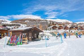 A ski resort with wooden buildings, a ski lift, and a snowy mountain backdrop.