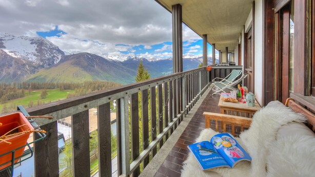 A balcony with a view of mountains, a wooden table with a book, and a white furry object. - La Stella Alpina in Sestriere (Sestriere)