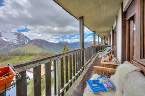 Een balkon met uitzicht op bergen, een houten tafel met een boek en een pluizig wit object.