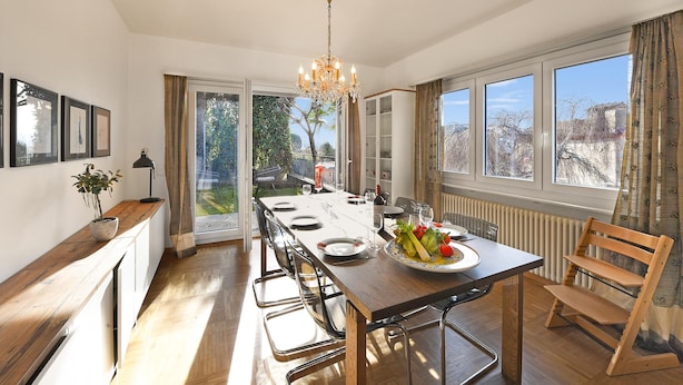Un comedor con mesa de madera, sillas, una lámpara de araña y vistas al exterior.