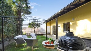 Un patio con mobiliario exterior, una parrilla y un pequeño jardín.