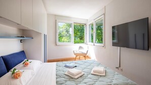 Une chambre d’hôtel moderne, dotée d’un grand lit, d’une télévision et offrant une vue sur la verdure par les fenêtres.