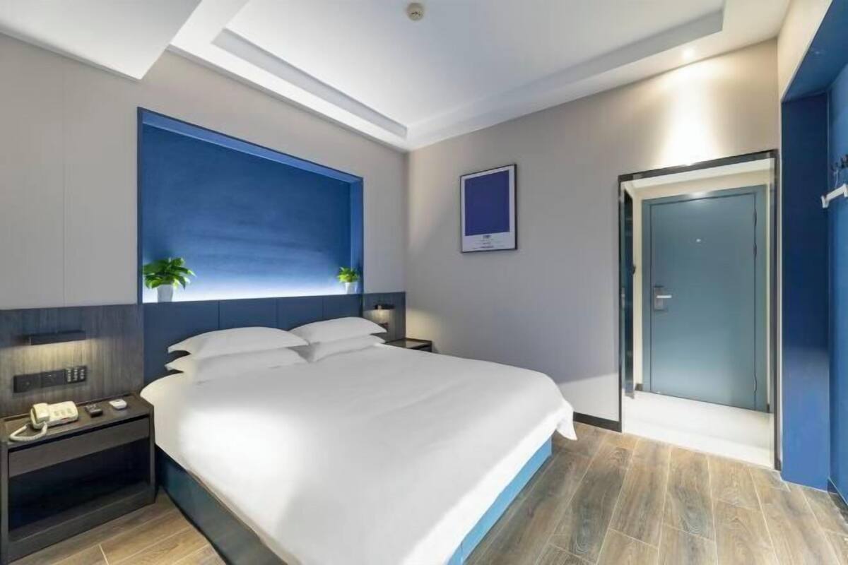 Ein modernes Hotelzimmer mit einem großen Bett, einem Nachttischtelefon, einem Beistelltisch und einem Fenster mit Aussicht sowie einer Tür.