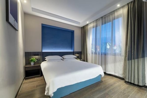 A modern hotel room with a large bed, a nightstand, a potted plant, and a view of the city through sheer curtains. - Yiman Hotel(Ningbo Passenger Transport Center) (Ningbo)