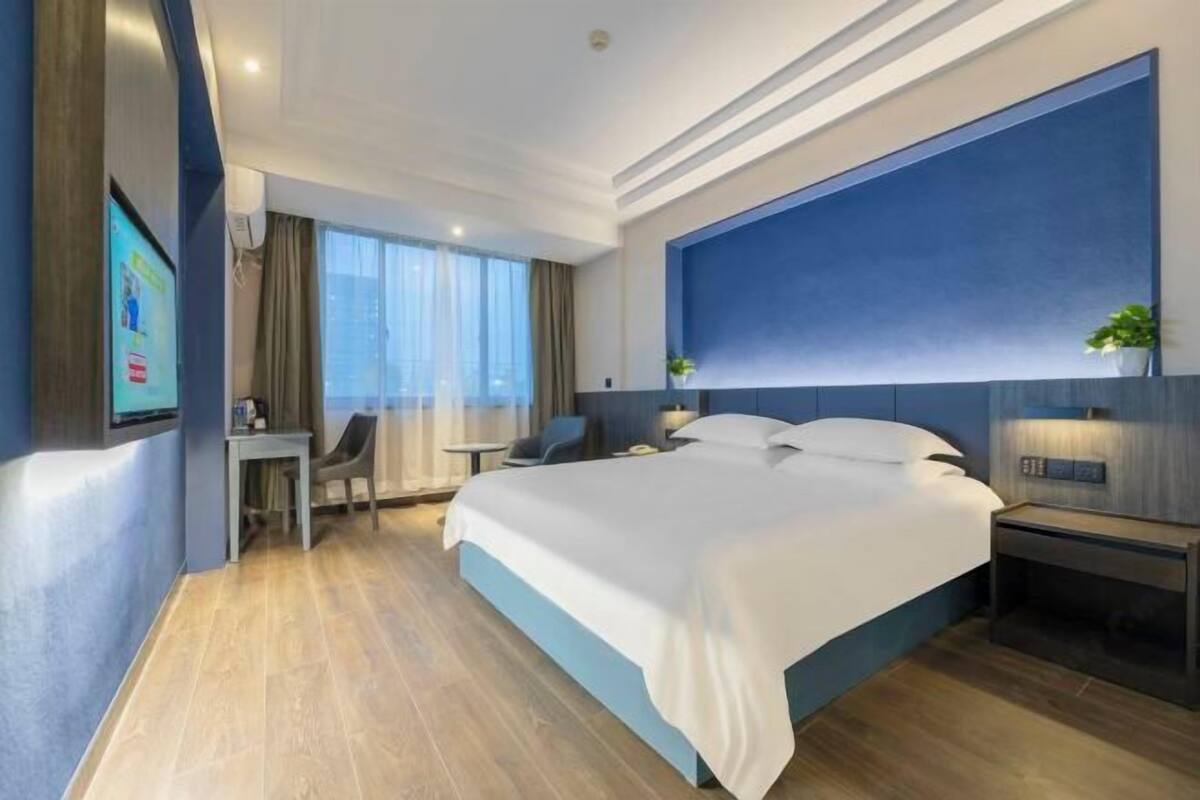 Ein modernes Hotelzimmer mit einem großen Bett, einem Schreibtisch, einem Sessel und einem an der Wand befestigten Fernseher.