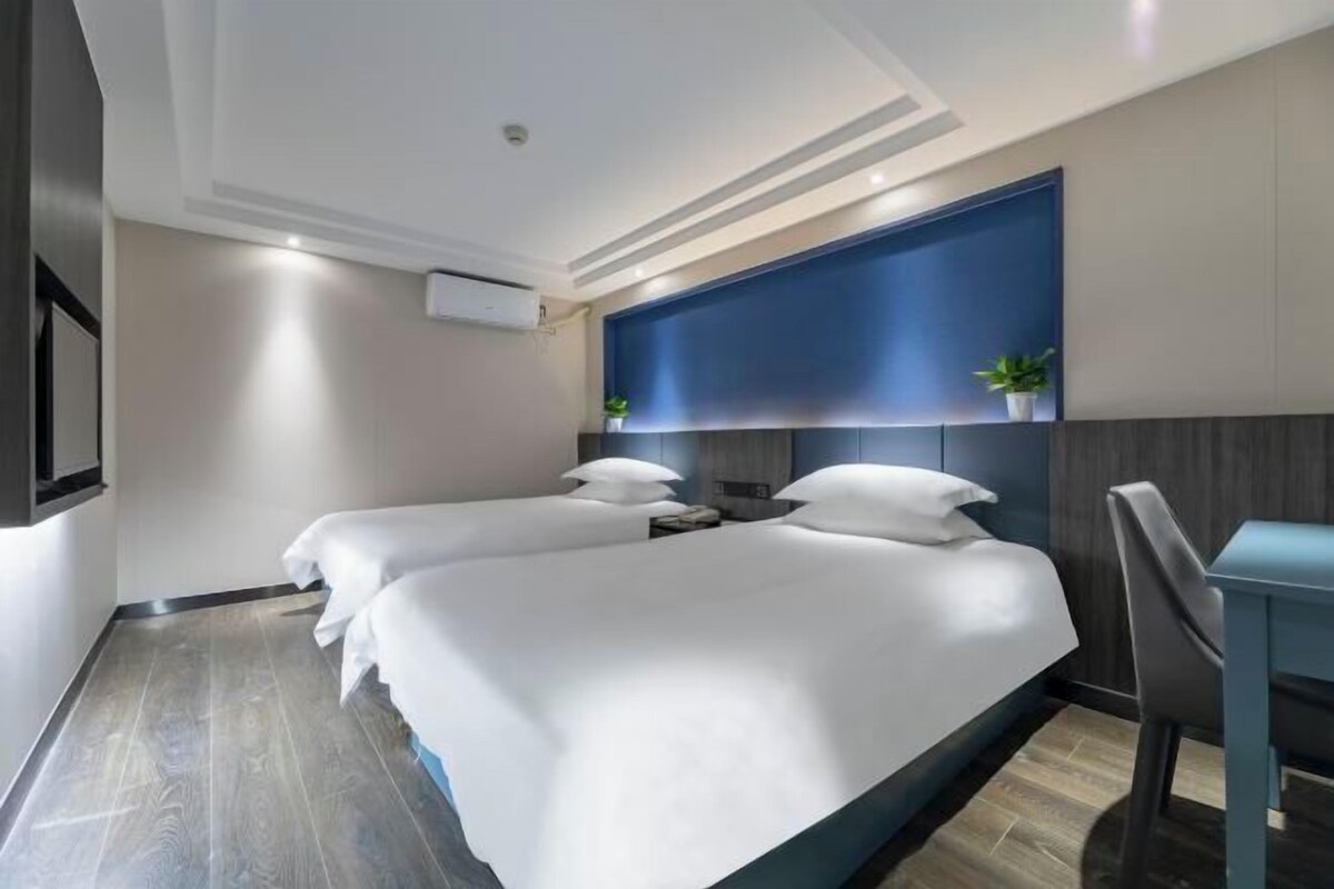 A hotel room with two beds, a desk, and a blue accent wall.