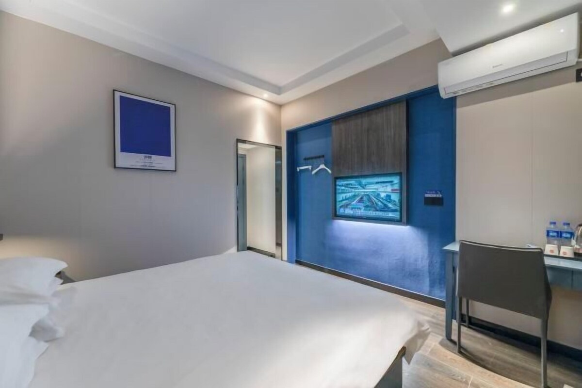 A hotel room with a bed, a desk, a chair, a TV, and an air conditioning unit.
