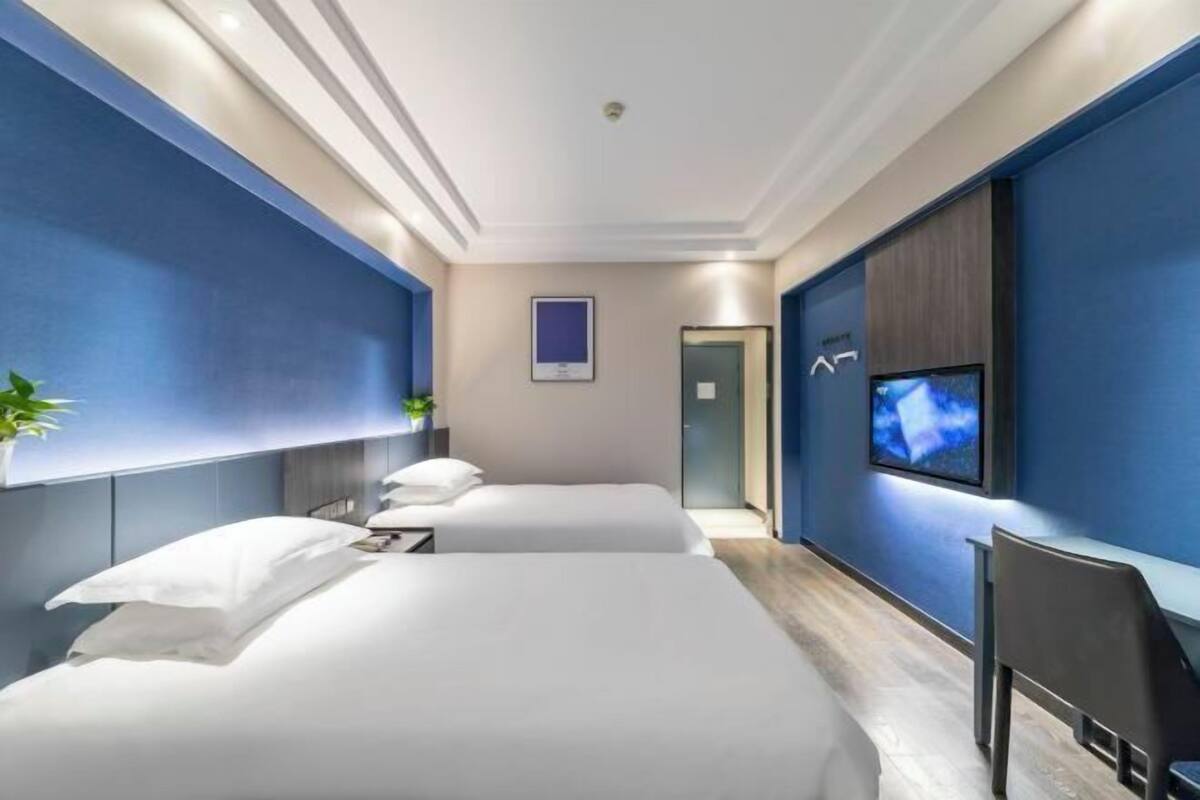 Ein Hotelzimmer mit zwei Betten, einem Fernseher, einem Schreibtisch und einer Pflanze.