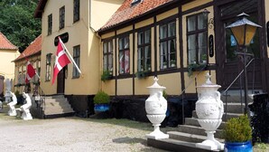 A traditional building with a tiled roof, a flag, and a staircase leading to the entrance. - 2-person Room in a Hotel in Tranekaer (Tranekaer)