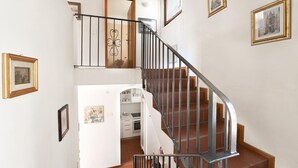 Una scala con ringhiera in metallo conduce a un piano superiore. Sui muri sono appese delle foto incorniciate e si intravede una zona cucina all'arrivo.