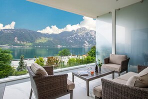 En balkon med fletningsmøbler, et bord og udsigt til en sø og bjerge.