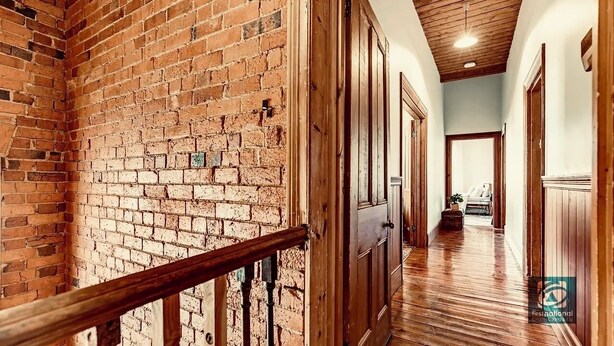 A hallway with brick walls, wooden doors, and a wooden railing. - Large, 2 BR stable conversion (circa 1874) tucked in the heart of old town. 🍃 (Echuca)