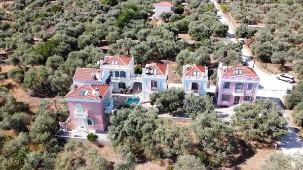 Eine Gruppe von Häusern im mediterranen Stil mit roten Ziegeldächern, umgeben von dichten Olivenhainen.