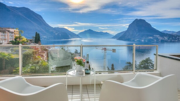 A balcony with a table, chairs, and a view of a lake with mountains.