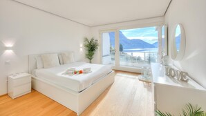 A modern bedroom with a large bed, bedside tables, a dresser, and a view of mountains through a large window.