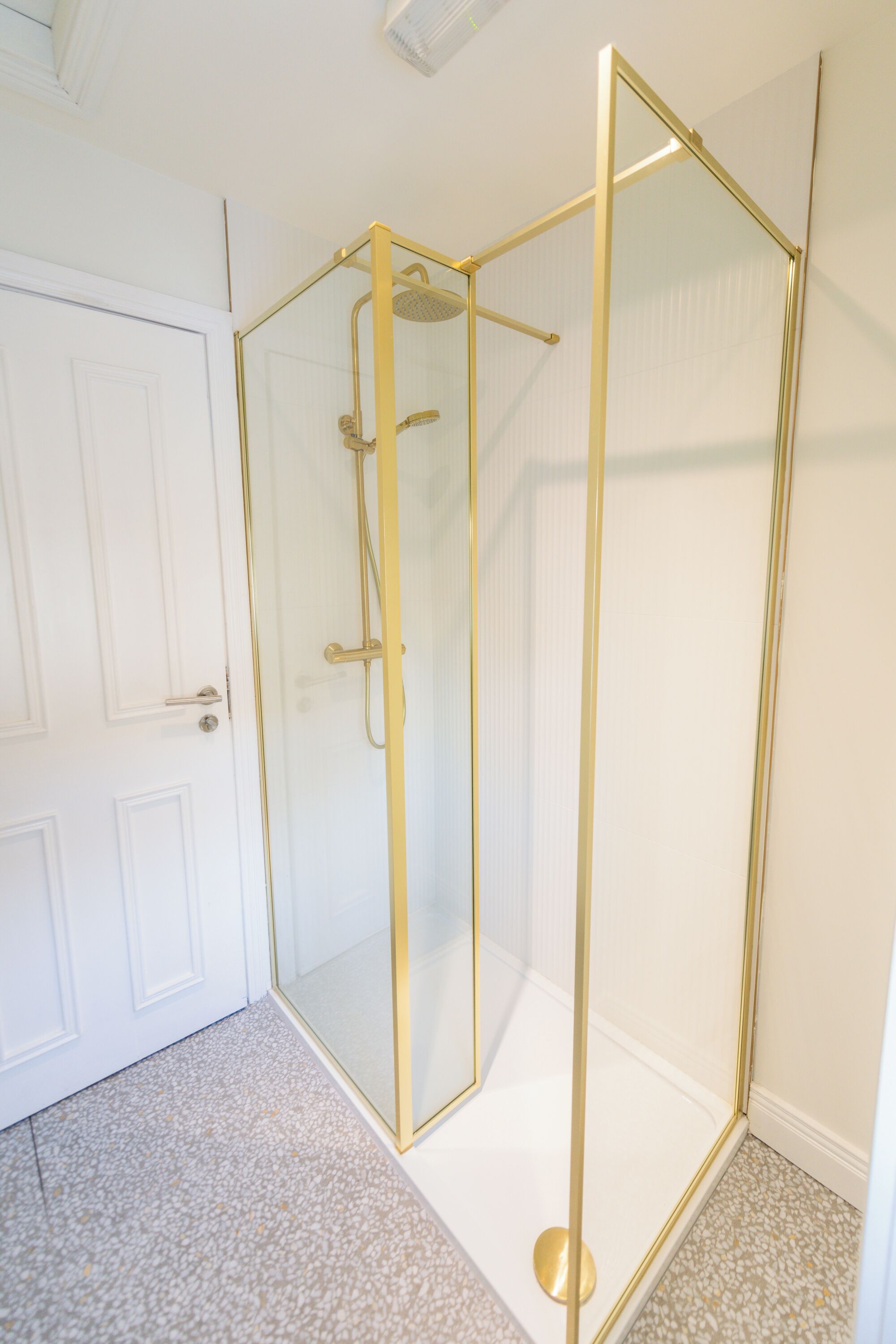 Une douche entièrementClose avec des éléments décoratifs dorés, une porte blanche et un sol à motifs.