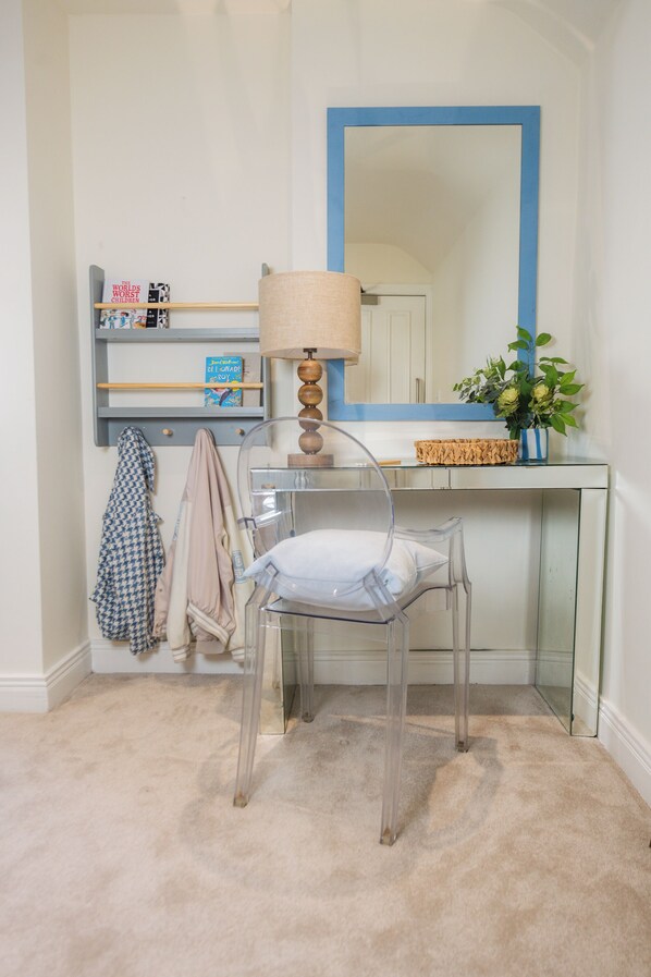 Un bagno con una sedia rotelle, uno specchio con cornice blu, una lampada e uno scaffale con libri e una pianta.
