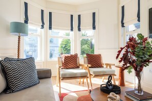 A cozy living room with a sofa, two armchairs, a lamp, a vase with plants, and a view of the outside through large windows. - Coastal Location - Sleeps 6 & Pet Friendly (Bangor)