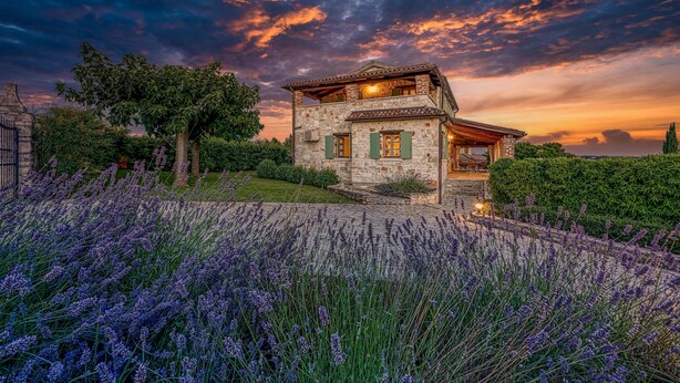 Une maison en pierre dotée d’un balcon, entourée de champs de lavande et d’un jardin.