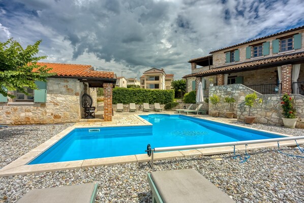Una piscina con borde de piedra, rodeada de guijarros y un seto.