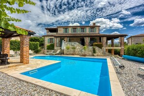 A two-story stone house with a swimming pool, outdoor seating, and a stone staircase.