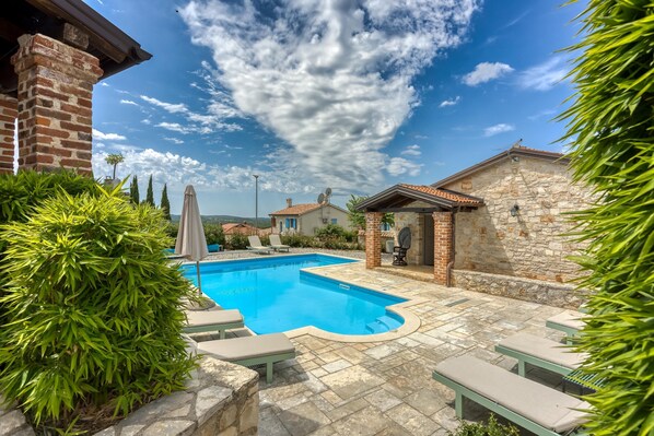 A swimming pool with a stone deck, surrounded by greenery and stone walls.