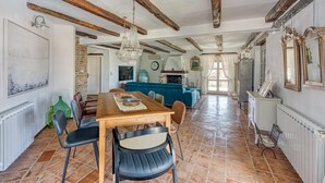 Un vaste espace dédié à la salle à manger, avec une table et des chaises en bois, un lustre et des poutres apparentes en bois au plafond.