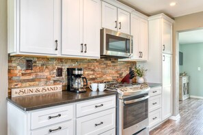A kitchen with white cabinets, a brick backsplash, a stainless steel range, and a microwave. - Tropical Escape (St. Augustine)