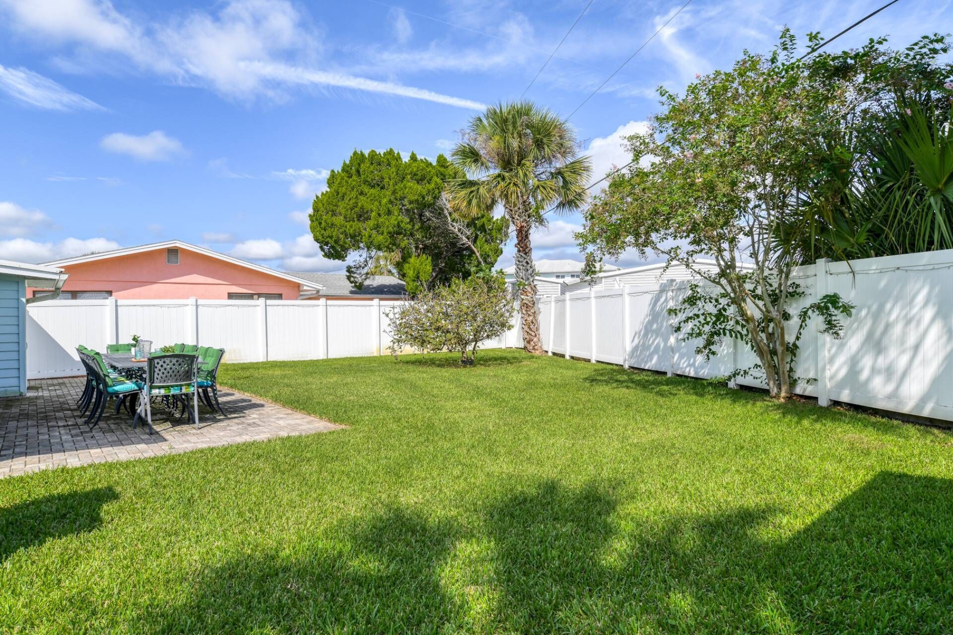 A backyard with a patio area, a white fence, and a palm tree.