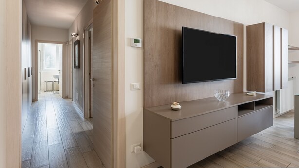 Ein modernes Wohnzimmer mit einem großen Flachbildfernseher an einer Holzvertäfelung, einem schlichten Konsolentisch und einem Gang zu einem weiteren Raum.