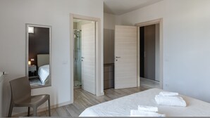 Ein modernes Hotelzimmer mit einem Bett, einem Sessel, einem Spiegel und einem begehbaren Kleiderschrank.