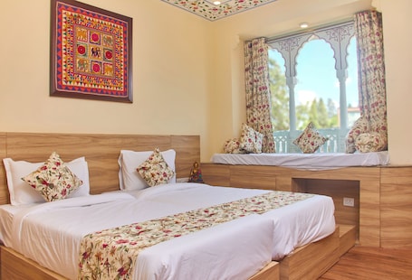 A neatly arranged bedroom with a large bed, floral-patterned bedding, a decorative wall hanging, and a window with ornate curtains.
