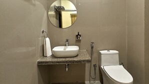 Ein modernes Badezimmer mit einem weißen Waschbecken, einem runden Spiegel, einer Toilette und einer Dusche.