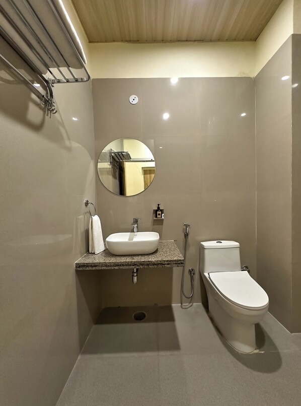 Une salle de bain moderne avec un lavabo blanc, un miroir rond, des toilettes et une douche.