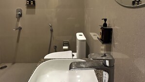 Ein Badezimmer mit weißem Waschbecken, einem Spiegel, einer Dusche und einem Handtuchhalter.