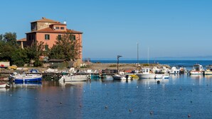 A coastal marina with boats docked, a prominent building with a tower, and a clear blue sky. - Sunset Populonia by Geco Vacation Rentals (Piombino)