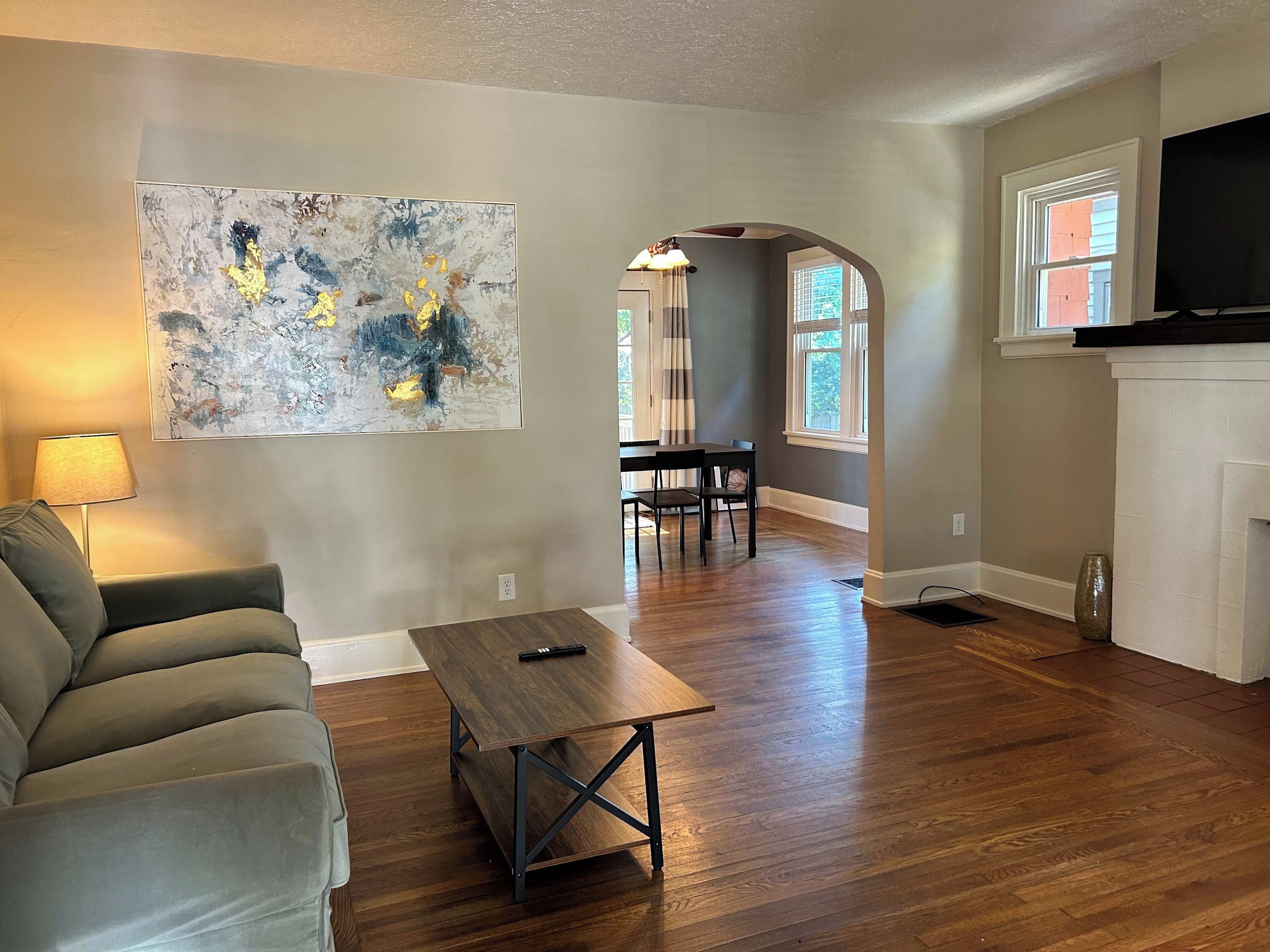A living room with a sofa, a coffee table, a painting, a dining area with chairs, a fireplace, and a TV.