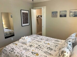 A bedroom with a bed, a mirror, a door, and three wall art pieces.