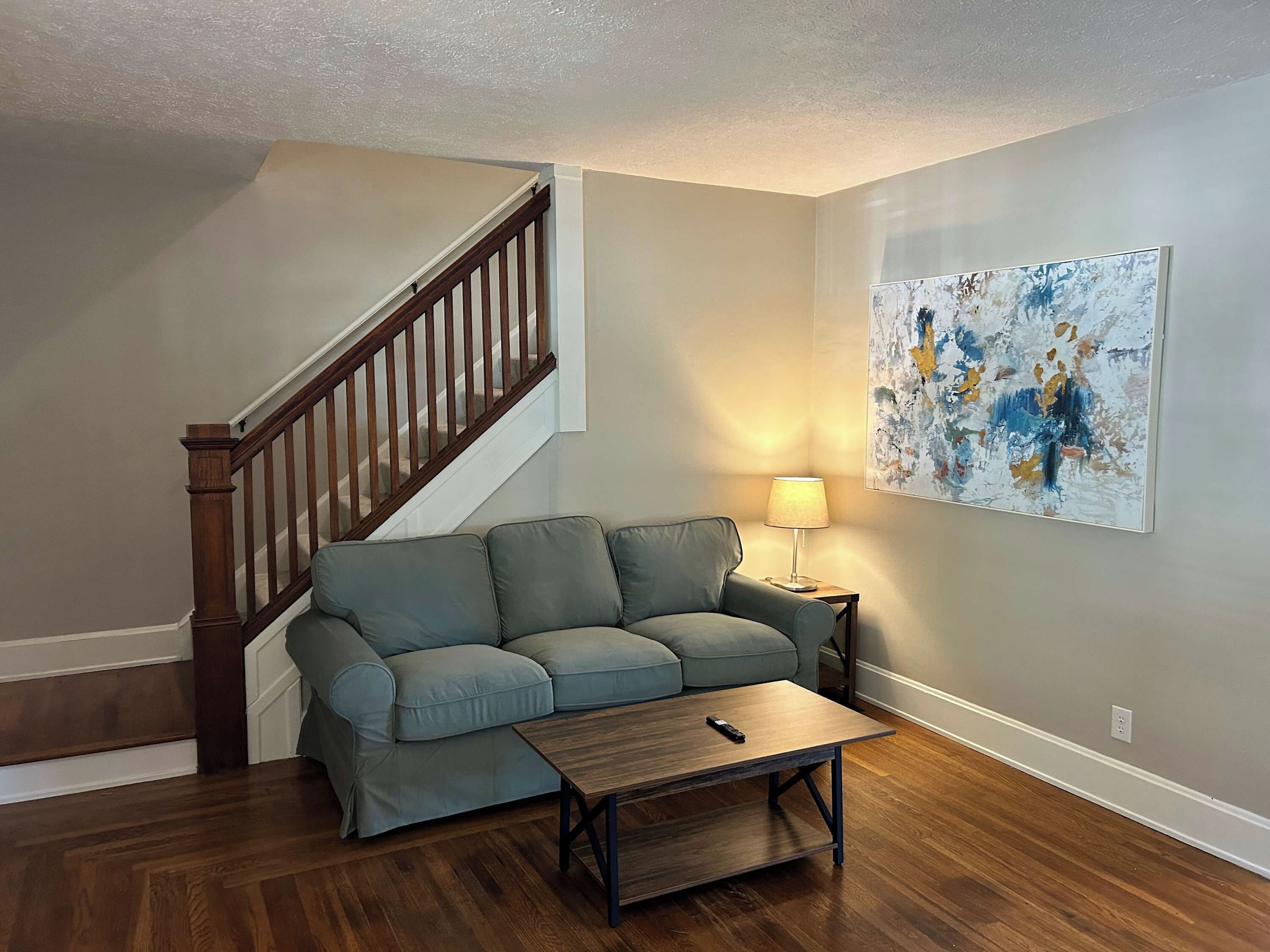 A living room with a wooden staircase, a gray sofa, a wooden coffee table, and a lamp.