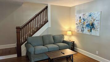 A living room with a wooden staircase, a gray sofa, a wooden coffee table, and a lamp.