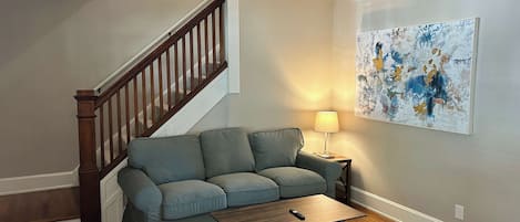 A living room with a wooden staircase, a gray sofa, a wooden coffee table, and a lamp.