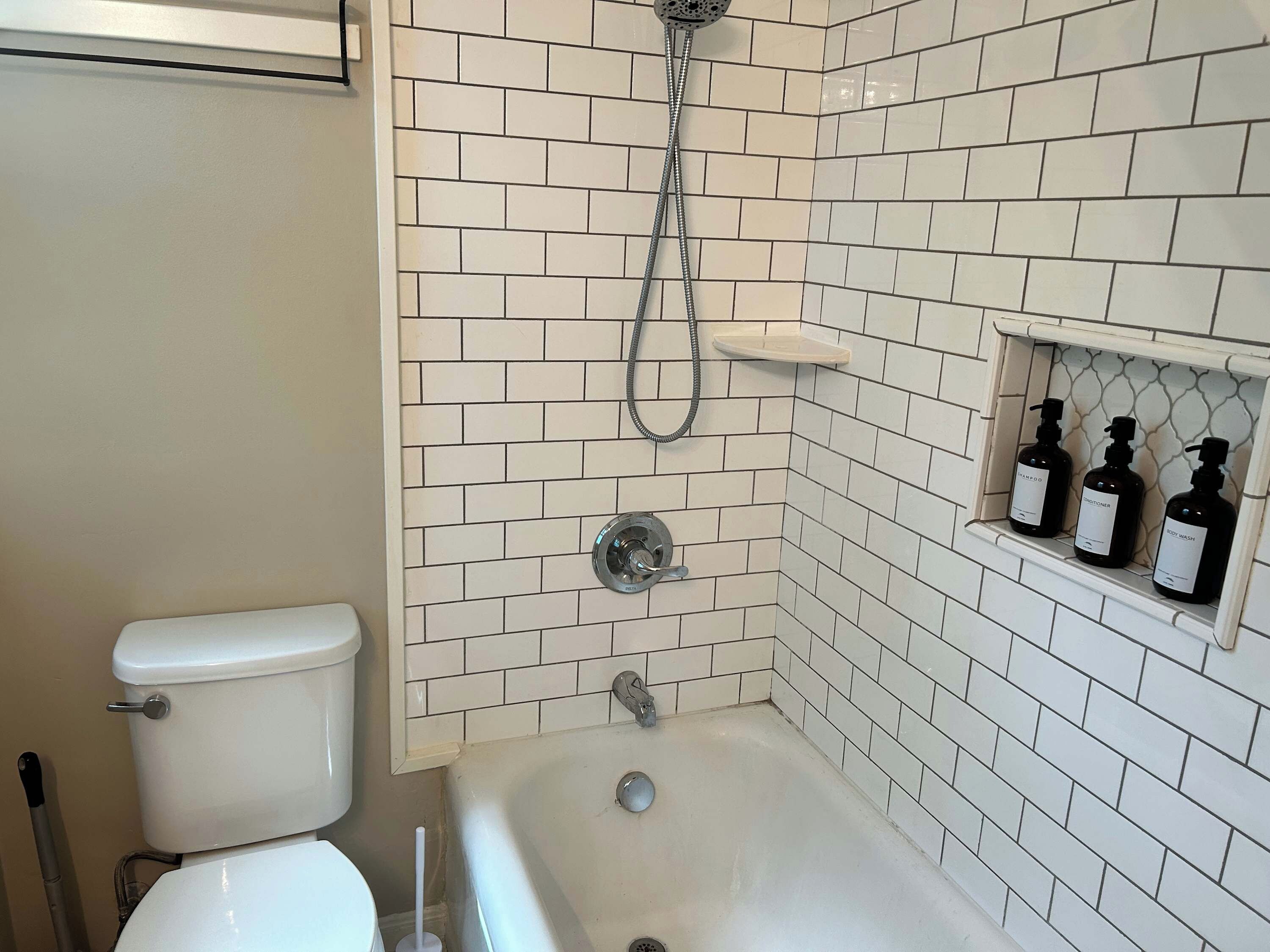 A bathroom with a toilet, a bathtub, and a shower. There are three bottles of toiletries on a shelf.