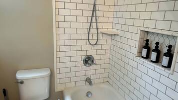 A bathroom with a toilet, a bathtub, and a shower. There are three bottles of toiletries on a shelf.