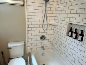 A bathroom with a toilet, a bathtub, and a shower. There are three bottles of toiletries on a shelf.