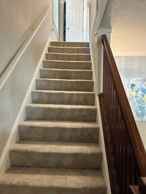 A carpeted staircase with a wooden handrail, leading to a room with a door. - Palmetto 2 Bed Family House in Cincy near Oakley (Cincinnati)