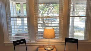 A room with two wooden chairs and a table with a lamp, positioned between three windows with blinds. - Palmetto 2 Bed Family House in Cincy near Oakley (Cincinnati)